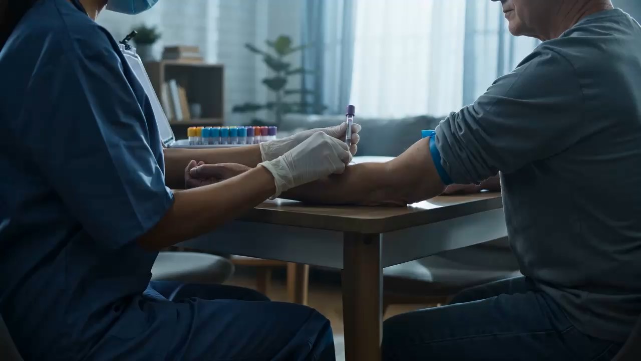 Flebotomista de Delihealth's tomando una muestra de sangre a una persona en la mesa de su casa.